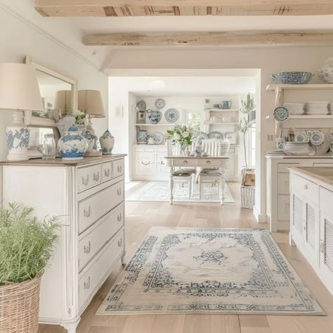 Created with Ai At the center of this kitchen lies a white and blue vintage rug, its intricate patterns drawing the eye and grounding the space. Surrounding it, white cabinets, their clean lines against the warmth of a wooden floor and delicate light wood ceiling beams. This kitchen is a celebration of summer, with plants that infuse the air with freshness and vitality. Atop the shelves, blue porcelain vases add a touch of sophistication, a dining table awaits, bathed in the soft glow of n... French Country Kitchens Blue, Vintage Blue And White Kitchen, Blue And White China Kitchen, Blue And White Vintage Kitchen, Blue And Cream Kitchen, French Cottage Core, Light Wood Ceiling, Blue And White Cottage, Hamptons Style Living Room