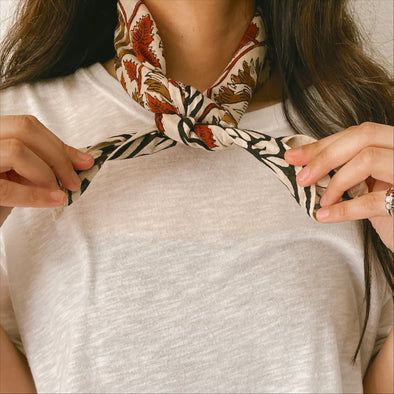 Close up of model tying a bandana around the neck. Ways To Fold Bandanas, Bandana With Outfit, Wearing A Bandana Around Neck, How To Tie Handkerchief Around Neck, How To Style Bandana Around Neck, Neck Kerchief Outfit, How To Tie Neck Bandana, How To Tie A Western Scarf, Neck Scarf Tie