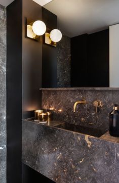 In this modern powder room, metallic accents have been paired with dark stone and black walls for a bold and dramatic appearance. #ModernPowderRoom #BathroomDesign Bathroom Without Windows, Modern Powder Rooms, Modern Powder Room, Glamorous Interiors, Dark Bathrooms, Powder Room Design, Bad Inspiration, Modern Toilet, Black Bathroom