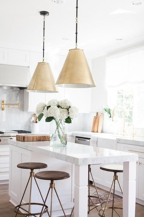 Two Goodman Hanging Lamps in Antique Brass hangs over a white kitchen island topped with gray and white quartzite lined with round brass and wood counter stools, Arteriors Wyndham Swivel Counter Stools. Kitchen Island With Stools, Island With Stools, White Kitchen Pendant Lights, Casa Open Space, Gold Kitchen Hardware, White Kitchen Lighting, Kitchen Gallery, Classic Kitchen, Kitchen Island Design