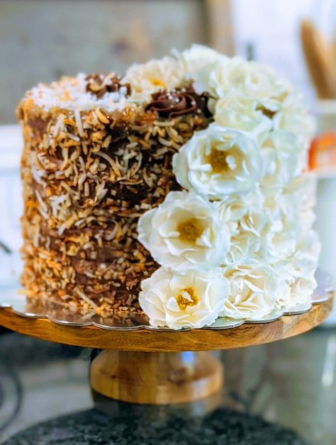 4 layer German chocolate cake, filled with chocolate buttercream and our brown sugar pecan frosting! A little toasted coconut and some fresh flowers top it all off! German Chocolate Anniversary Cake, Decorate German Chocolate Cake, German Chocolate Cake Wedding, German Chocolate Wedding Cake Ideas, Fancy German Chocolate Birthday Cake, German Chocolate Cake Designs, German Chocolate Cake Decorated, German Chocolate Wedding Cake, Chocolate Anniversary Cake