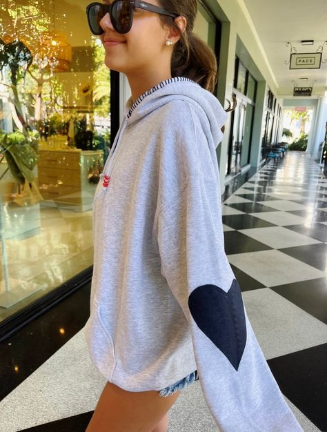 Our Heart Patch Hoodie comes in light grey with navy blue heart patches and navy sewing on the hood. The hoodie also has heart beads on the string. Hoodie runs true to size.