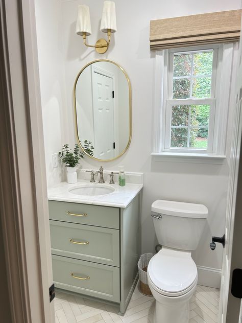 Transitional style powder bath designed by Delphinium Design in Charlotte, NC featuring a light sage green vanity, herringbone floor tile, gold oval vanity mirror, gold sconces and gold hardware  #powderroom #transitionalbathroom #transitionaldesign #DelphiniumDesign Sage And Brass Bathroom, Light Green Vanity Bathroom, Light Green Bathroom Vanity, Sage Green And Gold Bathroom, Sage Green Vanity Bathroom, Sage Green Powder Room, Sage Bathroom Vanity, Vanity Countertop Ideas, Sage Green Vanity