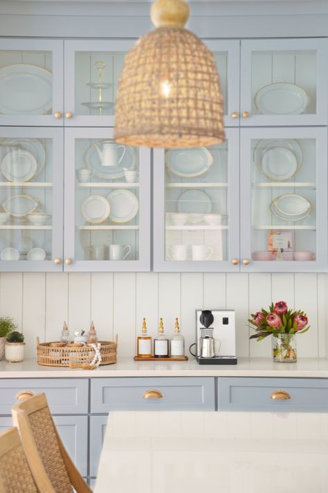 This image is of a coastal kitchen with light blue open cabinetry and white countertops and woven details such as barstools, decorative items, and lighting. This is the perfect coastal kitchen oasis! Country Beach House, Coastal Kitchens, Coastal Kitchen Ideas, Summerville Sc, Cornish Cottage, Light Blue Kitchens, Coastal Kitchen Design, Coastal Kitchen Decor, Baths Interior