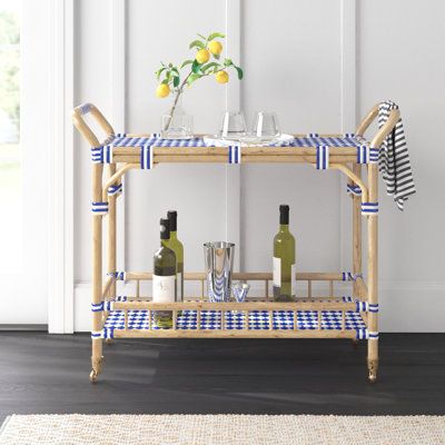 This bar cart offers a stylish way to serve up drinks and snacks, whether you're hosting a gathering or enjoying a relaxing evening at home. The solid bamboo frame features a light brown finish, while the top and bottom shelves showcase woven blue-and-white acrylic detailing for a coastal vibe in your space. With four wheels and two handles, this cart is easy to move around, and the included towel bar ensures you always have a cloth handy for spills. The cart's 50 lbs. weight capacity allows for Bar Cart Wood, Bar Corner, Wood Bar Cart, Serving Cart, Relaxing Evening, The Company Store, Bar Art, Florida House, Bamboo Frame