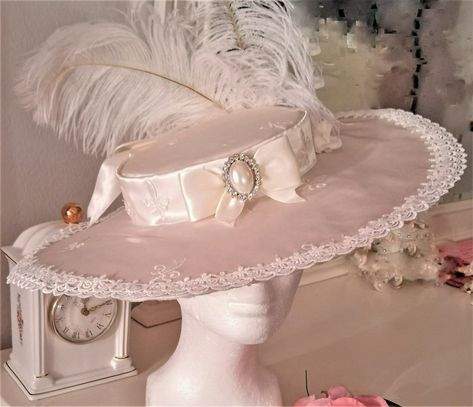 Belle Epoque Style Ladies Kentucky Derby Hat in a luminous Cream Taffeta w/ Fleur de Lis embroidery, ivory lace edging, faux pearl and Swarovski Crystal Front Brooch & Ostrich Plumes. This hat has a French sensibility, with 16 inch diameter and a crown diameter of 7 inches. Of it's many virtues, this hat is extremely versatile for a costumer, covering several fashion periods efortlessly ( Belle Epoque, Rococo, Georgian or Early Modern.) Kentucky Derby Style, French Hat, Rococo Fashion, Satin Ribbon Bow, Kentucky Derby Hat, Derby Hat, Fancy Hats, Derby Hats, Fantasy Fashion