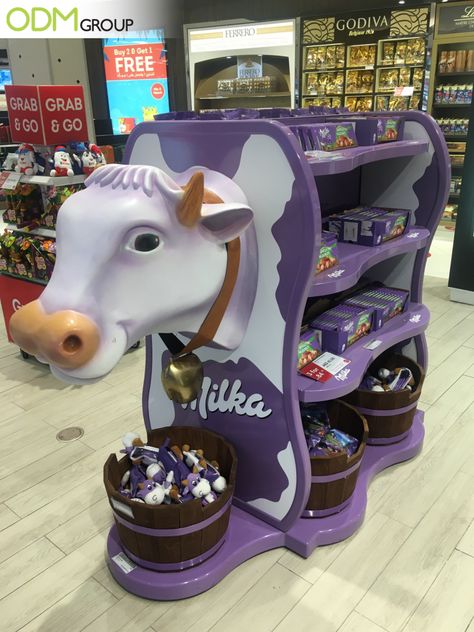 What brand comes to mind when you see a purple cow display inside the store? We automatically associate it with the chocolate brand Milka, correct? One of our staff members has recently come across their retail marketing display at a Duty-Free shop. The signature purple display is a head-turner! #POS #display #unique #eyecatching #catchy #design Milk Display, Retail Display Design, Toy Shop Display, Duty Free Shop, Shopper Marketing, Retail Design Display, Grocery Store Design, Retail Marketing, Snack Shop