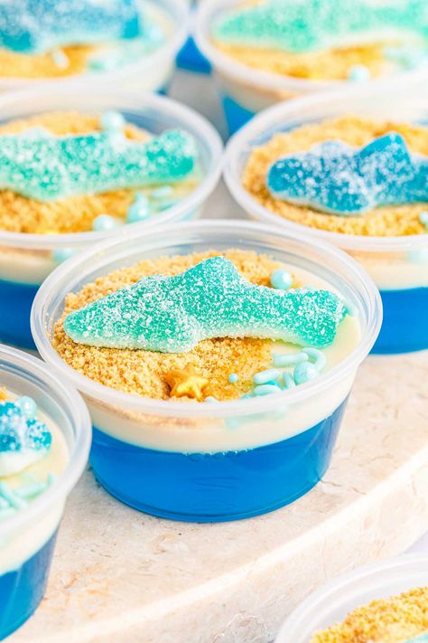 The best shark jello cups recipe - perfect for shark week or World Oceans Day with a gummy shark on top! Under The Sea Jello Cups, Ocean Jello Cups, Blue Jello With Fish, Obx Themed Snacks, Shark Themed Charcuterie Board, Shark Deserts, Shark Week Treats, Shark Jello Cups, Under The Sea Themed Food