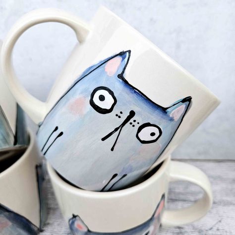 This listing is for one on my hand painted blue/grey cat mugs. Painted by hand, by me. Each mug is entirely unique. Once painted, it's then fired in the kiln, before being glazed and fired in the kiln again. This mug is hand painted and hand glazed so may contain small marks or imperfections making it totally unique. It is dishwasher and microwave safe, although I would recommend handwashing. Mug size is: 10.1cm D x 9.5 cm Height, holding 12oz of liquid (which is a big, but not *too* big cup of Painting On Cups Mugs, Paint A Mug Ideas, Mugs Painting Ideas, Cat Pottery Painting, Hand Painted Pottery Mugs, Pottery Painting Mug Ideas, Cup Designs Ideas, Mug Painting Ideas Easy, Rainbow Ceramics