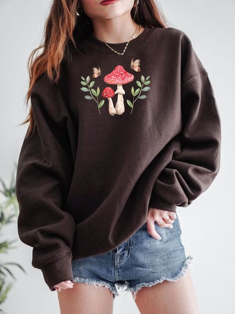 Enjoy the Cottagecore Aesthetic with this cute Mushroom Sweatshirt! This Cottage Core Mushroom Sweater is super comfy! Size up for a Trendy Oversized Look! Makes the perfect gift for that special Mushroom Lover in your life! ♥ Hello and Welcome to Meaningful Tees Shop! ♥ Printed on the most popular Unisex Sweatshirt, the Gildan 18000 is 50% Cotton / 50% Poly. The soft fleece lining makes it super Comfy and is sure to become your new favorite! ♥ All of our items are made one at a time with care for each customer : ) ♥ Please allow 3-7 BUSINESS days (usually 4-5) for your item to be created PLUS shipping time via USPS ♥ This Unisex Sweatshirt fits like a Men's on Women, but is not overly large. ♥ For a RELAXED FIT, your usual size will typically work, but please consult the Size Chart in the Mushroom Embroidery Sweater, Cottage Core T Shirt, Cottage Core Trousers, Mushroom Outfit Aesthetic, Mushroom Aesthetic Outfit, Nature Clothes Aesthetic, Mushroom Core Aesthetic, Cute Shirts Aesthetic, Grunge Cottagecore Outfits