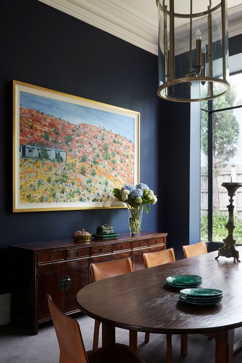 This traditional home was given a colourful makeover! Done by the team at Brownlow Interior Design, this beautifully restored period home was updated using a bold colour palette. This dark blue dining room features a dark wood dining table, leather chairs, green plates, grogeous abstract landscape artwork and a stunning dark brown wood cabinet on the side. To find the full home tour, click on the pin or go to StyleCurator.com.au. Victorian Italianate House, Dark Blue Dining Room, Dark Wood Dining Room, Decorating With Antiques, Italianate House, Antique Bedside Tables, Dark Wood Dining Table, Maple Dining Table, Dark Dining Room