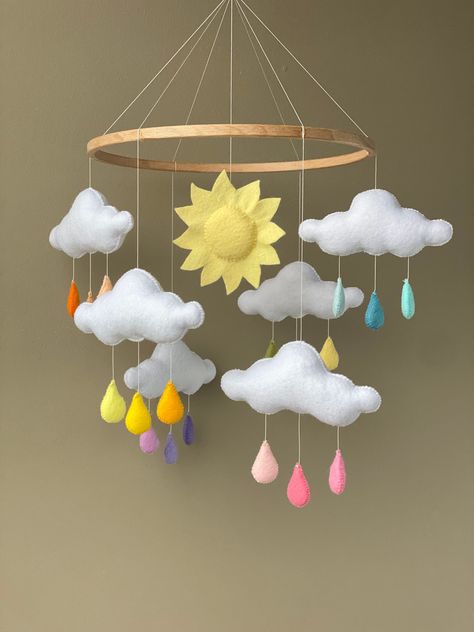 Rainbow rain cloud baby mobile for the sunshine nursery. This mobile is well suited for the baby girl or boy and will be great for a new baby shower gift and the perfect decor for the baby rainbow nursery. Individual design is possible. Just ask me if you want to change any detail of the mobile. 🌦BABY MOBILE INCLUDES  - 6 clouds with rainbow drops and the sun  - the wooden hanger with toys Additional you can add to your order crib mobile hanger with music box (see link below) https://www.etsy.com/your/shops/SKLcraft/tools/listings/735667820?ref=listing_card_body&from_page=/your/listings 🌦MATERIALS  - eco-friendly high-quality felt -  hollow fibre filling - nylen threads 🌦THE SIZE  Width - 22 cm ( 8.66 inch) 🌦CARE INSTRUCTIONS  Simple care instructions for felt mobile's toys:  - Dry cle Rain Cloud Nursery, Clouds With Rainbow, Rainbow Nursery Theme, Felt Weather, Weather Mobile, Sun Nursery, Rainbow Baby Nursery, Sunshine Nursery, Felt Baby Mobile