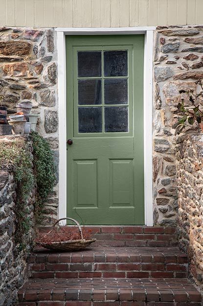 Brick stairs leading up to a green front door surrounded by stacked stone. Yellow Door Green Shutters, Green Front Door Stone House, Front Door Colors With Stone House, Dark Gray House With Green Door, Brick House With Painted Front Door, Yellow House With Green Door, Green Door Cottage, Green Paint For Front Door, Sage Green Front Door Tan House