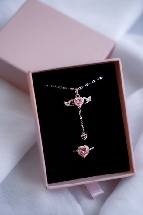 Discover the elegance and romance of our Heart's Desire Jewelry Set! This stunning set includes a delicate necklace and a matching ring, both showcasing exquisite heart-shaped pink gemstones surrounded by brilliant clear stones. The necklace features a lovely winged design on either side of the pendant, symbolizing freedom and beauty, and a little dangling heart for added charm. The ring echoes this design, with a striking heart-shaped pink gemstone embraced by sparkling clear stones. ✨ **Unique Tangled Jewelry, Ring Gift Box, Unique Valentines Day Gifts, Pretty Jewelry Necklaces, Magical Jewelry, Jewelry Accessories Ideas, Heart Gemstone, Set Necklace, Pink Necklace