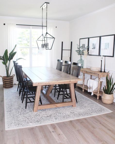 Light wood dining table is accented with black spindle back dining chairs under a black linear lantern light. Gray and beige vintage area rug for kitchen table is laid underneath the table covering stained wood flooring. Dining Table With Grey Floor, Light Table Dark Chairs Dining Room, Dining Table With Black Spindle Chairs, Dining Room Table With Grey Floors, Light Wood Dining Table Decor, Rug Under Dining Table Or Not, Dining Table For Light Wood Floors, Combined Dining Room And Living Room, Light Gray Rug Living Room