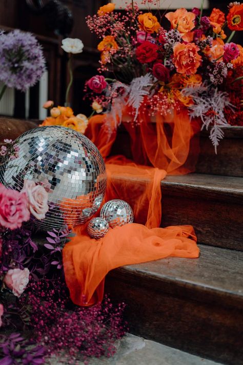 Large disco ball wedding decor on orange tulle fabric and colourful flower arrangements with pink garden roses, purple giant alliums, dark red poppies and foliage Brighton Wedding Venues, 70s Bride, Wedding 70s, Disco Ball Wedding, Orange Purple Wedding, Groovy Wedding, Retro Wedding Theme, Wedding Disco, Orange And Pink Wedding