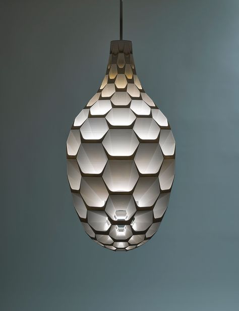 3d-printed chandelier, inspired by nature, using hexagonal geometry and bioplastic material, precisely shaped to produce distinctive, glare-free illumination. The Hedron Pendant is defined by a filigree-like 3d-printed shade, delicately wrapped around a stem with LED source.  The shade is an array of tapered cell walls, precisely angled to bounce light twice from the internal LED source to the softly diffused light exiting the fixture. The 3d-printed bioplastic surfaces have a subtle, striated texture creating a distinctive gradient across each surface.  With a translucent white natural color, the fixture has an ethereal quality by day and a uniquely warm quality of light by night. With the optional white ceramic coating, the fixture takes on a more dramatic quality of light, with strong g Chandelier Drawing, 3d Printed Pendant, Tiered Seating, Chandelier Led, 3d Printing Diy, Modern Residence, Lighting Lamp, Indirect Lighting, Honeycomb Design