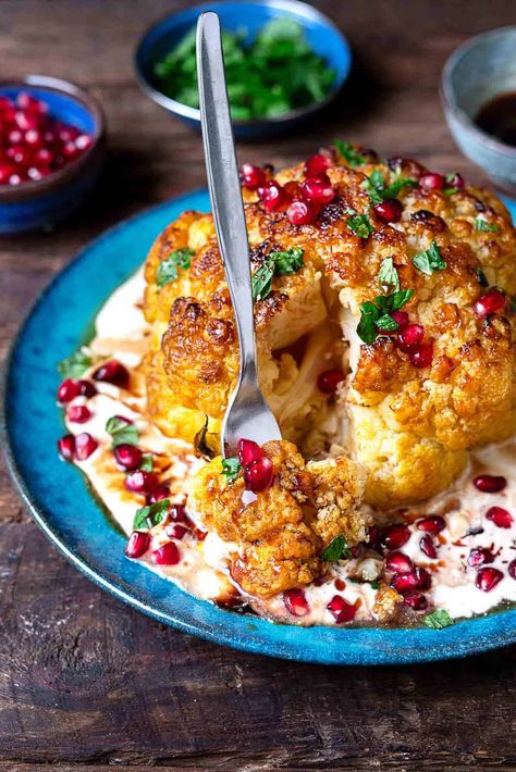 a whole roasted cauliflower with feta and yogurt sauce topped with pomegranate dressing and mint leaves on a plate being cut into by a fork. Mediterranean Veggies, Veggies Roasted, Charred Cauliflower, Appetizer Table, Pomegranate Recipes, Roasted Cauliflower Recipes, Cauliflower Dishes, The Mediterranean Dish, Whole Roasted Cauliflower