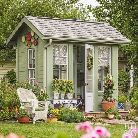 This cottage potting shed takes design cues from the main house, using the same earthy green and white paint colors. Extras like a deck, stone path, and cottage-style mixed planting borders make the backyard shed design feel more like a home than just an outbuilding. Several garden shed decorating ideas, like lace curtains in the windows, a quaint bench, and outdoor art also add homey appeal. In a practical move, downspouts ensure rains don’t damage the plants that surround the building. Shed Inspiration, Small Garden Shed, Backyard Sheds, Backyard Shed, Potting Sheds, Stone Path, She Sheds, Diy Shed, Shed Design