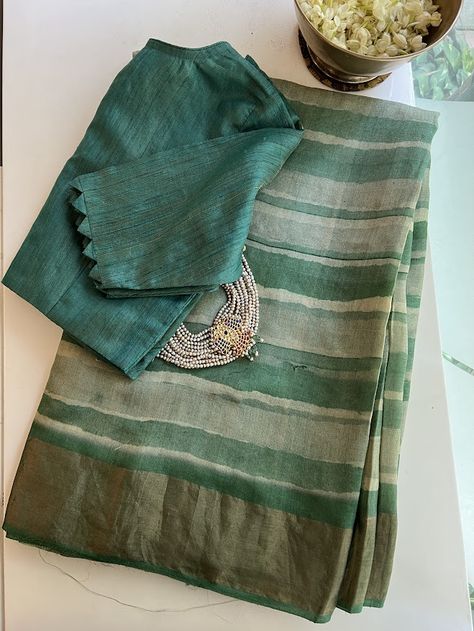 This dreamy saree is crafted from raw and lustrous pure handwoven tussar silk. Handprinted bands of green-hued stripes emulate the fluidity and translucence of watercolors and the deepsea. The addition of pure zari borders and a zari-striped pallu enhances the elegance of this sophisticated and ethereal drape. The saree comes with a floral printed green and beige blouse piece that is the perfect yin to the yang. Fancy Blouses Designs, Dreamy Saree, New Dress Design Indian, Ikat Blouse Designs, Pure Tussar Silk Saree, Jute Silk Saree, Saree Jacket Designs, Saree Styling, Tussar Saree