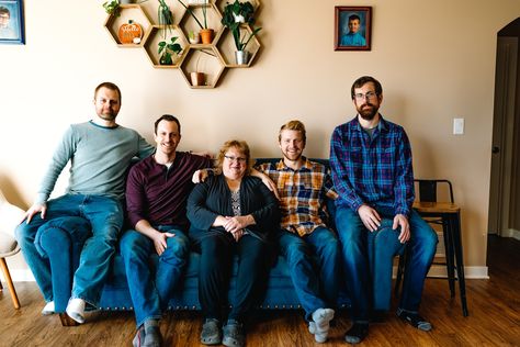 Des Moines, Iowa family photography - a mother sits on a blue couch flanked by her four adult sons inside for family photos. Family Photos