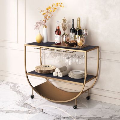 The sleek MDF top not only offers a contemporary allure but also provides a functional surface for serving cocktails, displaying decor items, or even holding your favorite books and accessories. The Reiney Bar Cart becomes a chic and mobile centerpiece for your creative expression and a perfect addition to your entertaining arsenal. | Everly Quinn Reiney Metal Bar Cart Wood / Steel in Brown / Gray / Indigo | 30.3 H x 39.4 W x 15.7 D in | Wayfair Wood Bar Cart Styling, Wine Apartment, Bar Cart Wood, Art Deco Bar Cart, Gold Bar Cart Styling, Bar Cart Ideas, Wine Lounge, Wine Glass Hanger, Coffee Bar Cart