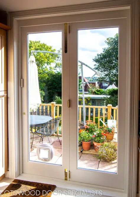 Stunning wooden bifolding doors with full double glazing, installed in a contemporary kitchen. The doors are fitted on a clever track system which enables them to slide fully open – ideal for opening up the kitchen to the garden on a beautiful day for al fresco dining on the patio. Painted white, these wooden bifolding doors frame a large and leafy view of the garden, lending the kitchen a real sense of spaciousness Doors To Deck From Kitchen, Kitchen Courtyard, Kitchen Patio Doors, Bifolding Doors, Double Patio Doors, Wooden Sliding Doors, Prairie Rose, Doors Kitchen, Double French Doors