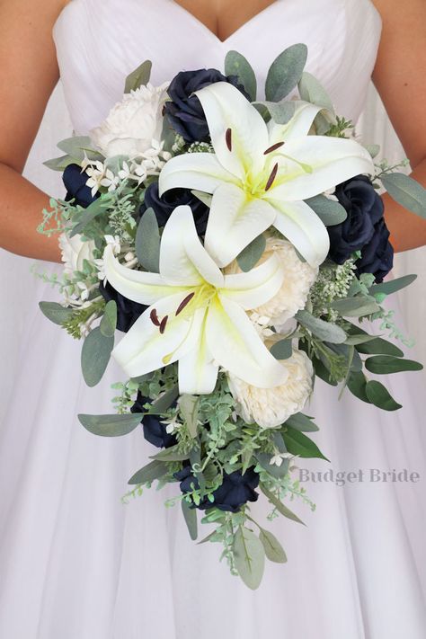 This brides’ bouquet is the perfect option if you have chosen a classic theme for your wedding. A lovely array of neutral white lilies and ivory peonies are center-stage in this stunning arrangement. Navy blue roses and greenery complete this romantic and beautiful design. As always, this bouquet has been wired by hand and designed by our in-house florists - you can rest assured that our bouquets will maintain their quality and stand the test of time for years to come. We never use foam to ancho Navy And Sage Wedding Bouquet, Lilly Bridal Bouquet Lilies, Rustic Elegant Wedding Bouquet, Shades Of Blue Wedding Bouquet, Hydrangea Lily Bouquet, Hydrangea And Lily Bouquet, Bridal Bouquet With Lilies, Wedding Bouquet With Lilies, Blue And White Wedding Bouquets