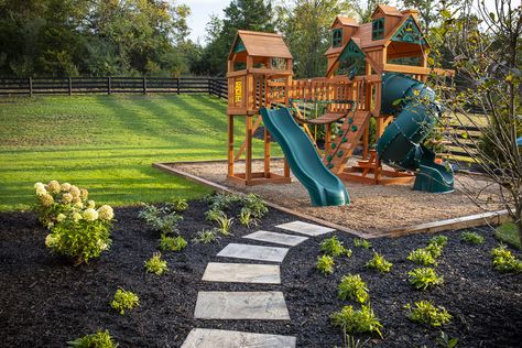 Outside children's playset and stepping stones Playset In Corner Of Yard, Play Set Landscaping Backyard Playground, Playset Landscaping Ideas, Backyard Design With Playset, Playground Area Landscape, Home Playground Landscaping, Mulch Play Area For Kids, Outdoor Playset Landscaping, Backyard With Playset