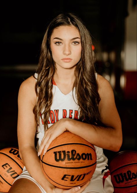 Girl sitting on basketball rack holding a basketball with a serious face. Senior Basketball Photography, Basketball Court Photography, Cool Basketball Pictures, Basketball Photoshoot, Basketball Team Pictures, Hoop Backdrop, Basketball Pictures Poses, Sports Photoshoot, Basketball Senior Pictures