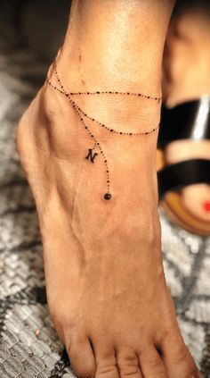 Tattoo Ideas Anklet, Name Charm Bracelet Tattoo, Ankle Bracelet Tattoo With Initials, Tattoo Ideas Female Leg Ankle, Ankle Bracelets With Names, Woman Ankle Tattoo Ideas, Tattoo Anklet Bracelet, Ankle Bracelet Tattoos For Women Wrap Around, Tattoo Ideas Ankle Anklets