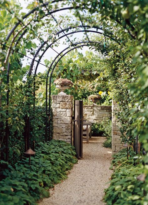 Arch trellises connected within a metal framework line up to create a tunnel that guides visitors from one area to the next. The striking construction frames a foliage-lined gravel walkway leading to a stone-walled outdoor room. #archtrellis #gardenarch #archwayideas #landscaping #bhg Metal Arbor, Garden Arch Trellis, Arch Trellis, Jardim Diy, Metal Pergola, Garden Vines, Garden Arbor, Garden Arches, Garden Entrance