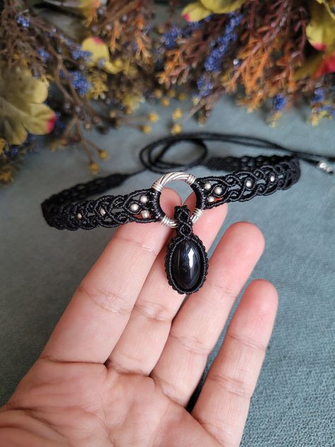 The macrame onyx choker in black is a unique and handcrafted accessory designed to make a statement. It showcases a meticulously hand-woven pattern using durable, high-quality black cord. At its center, the choker features a smooth, lustrous onyx gemstone known for its deep black color and subtle shine, symbolizing protection and strength.The design of the choker combines traditional macramé techniques with contemporary style, resulting in a piece that is both timeless and trendy. The intricate Macrame Choker Pattern, Macrame Choker Necklace, Choker Patterns, Jewelry Diy Ideas, Macrame Choker, Choker Necklace Black, Macrame Jewelry Tutorial, Macrame Bracelet Patterns, Black Macrame