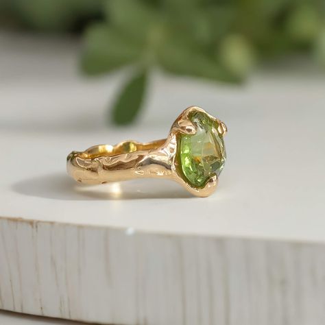 A beautifully handcrafted Peridot engagement ring, uniquely made with wax and cast in solid 14k gold. Its textured band lends a rustic charm to the elegant green stone, captured in a mesmerizing light play. This August birthstone ring is more than just jewelry—it's a poetic expression of individuality and lasting love, perfectly embodying your unique story. Available in sterling silver or solid 14k gold. Engagement Rings Natural Stone, Light Green Ring, Ethereal Rings, Ethereal Engagement Ring, Rings Engagement Unique, Peridot Ring Engagement, Organic Engagement Ring, August Jewelry, Green Wedding Ring