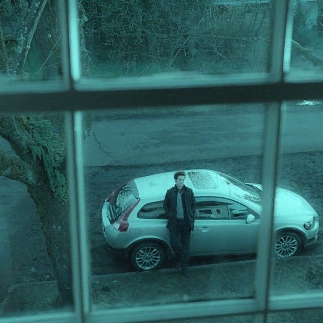 a man standing next to a parked car in front of a window on a rainy day