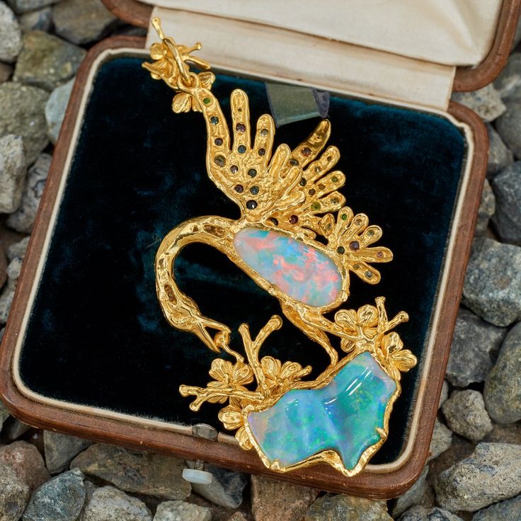 This stunning pendant features a bird and flower design, bezel set with two (2) opal cabochons. The flowers are each four-prong set with one (1) round mixed cut hessonite garnet. The eye of the bird is flush set with one (1) round mixed cut ruby. The feathers of the bird are flush set with a total of twenty- five (25) round mixed cut tourmaline and seventeen (17) round mixed cut demantoid garnets. The pendant measures 90.0mm long, including the bail and 40.0mm wide. The chain in the photo is not Luxury Hallmarked Opal Jewelry, Luxury Opal Cabochon Jewelry, Elegant Multi-stone Opal Jewelry, Elegant Ethiopian Opal Cabochon Jewelry, Elegant Ethiopian Opal Jewelry With Cabochon, Formal Ethiopian Opal Cabochon Jewelry, Exquisite Collectible Jewelry Brooch, Exquisite Collectible Brooch Jewelry, Luxury Ethiopian Opal Formal Jewelry