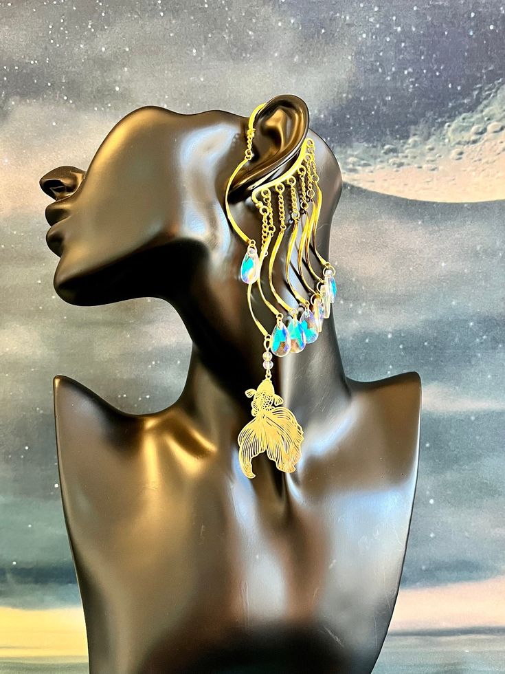 This enchanting water guardian ear cuff is sure to make a statement and bring out your inner magic! Gold ear cuff wrap is embellished with a light filigree gold fish charm and iridescent colorful glass drops dangling from wavy connectors and gold chains. This ear cuff is lightweight and perfect for adorning pierced and non-pierced Your jewelry is always wrapped in a jewelry bag and ready to be the perfect unique gift for yourself or someone you love! 💛 Fish Earrings Gold, Unique Drop Cartilage Earrings, Unique Dangle Cartilage Earrings, Nickel-free Metal Dangle Ear Cuff, Nickel Free Metal Dangle Ear Cuff, Whimsical Brass Dangle Jewelry, Fantasy Style Single Earring For Festival, Metal Dangle Ear Cuff, Metal Dangle Ear Cuff Single Earring