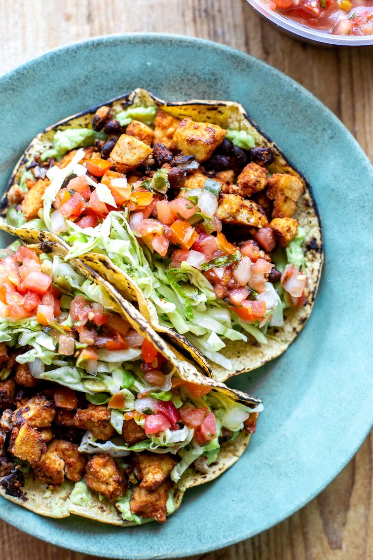 two tacos on a blue plate with salsa and tofu in the back ground