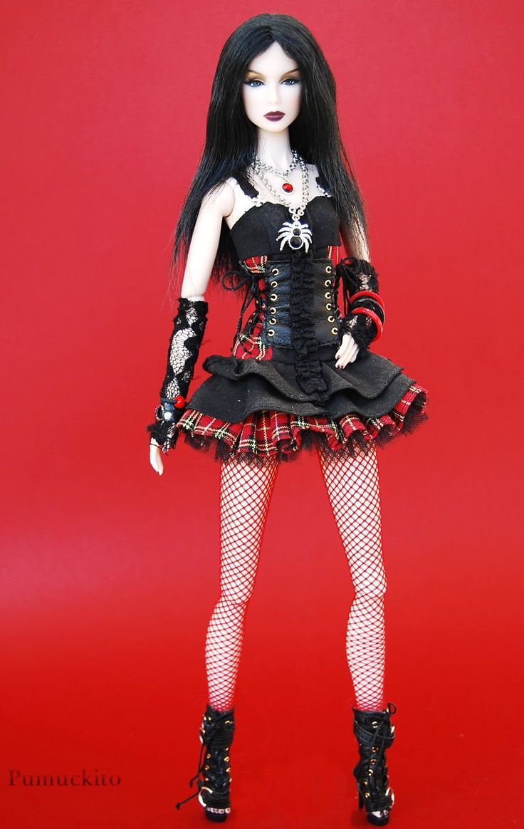 a doll dressed in black and red is standing on a red background with her hands behind her head