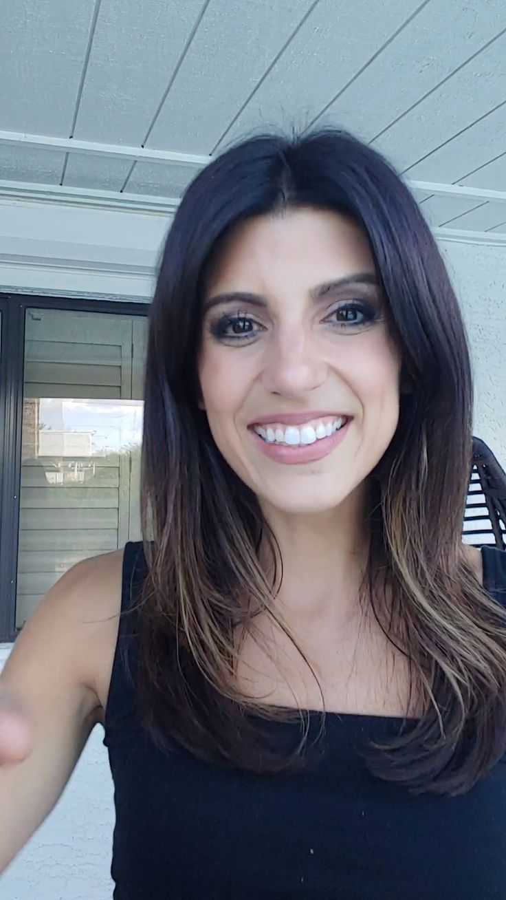 a woman with long dark hair is smiling and holding her hand out to the side