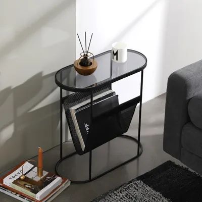 a glass table with magazines on it next to a gray couch and coffee cup in the corner