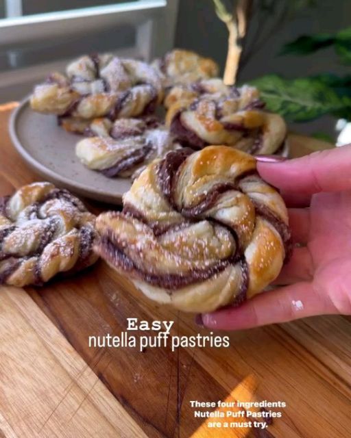 a person is holding up some food on a wooden cutting board with the words easy nutella puff pastries