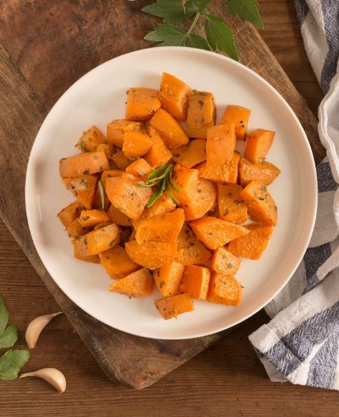 a white plate topped with cooked carrots on top of a wooden cutting board