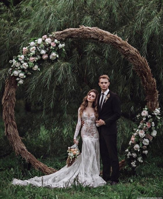 a man and woman standing in front of a circular wooden arch with flowers on it