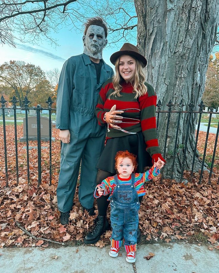 a woman and child dressed up in costumes standing next to a tree with a creepy face on it