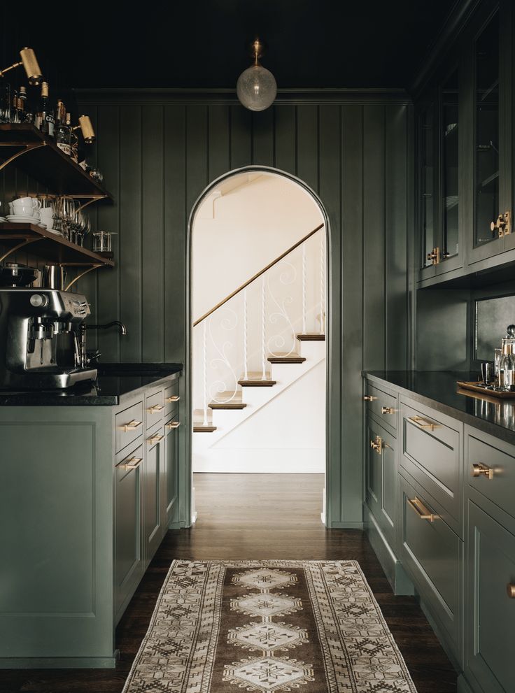 a kitchen with green cabinets and an area rug in front of the door that leads to another room