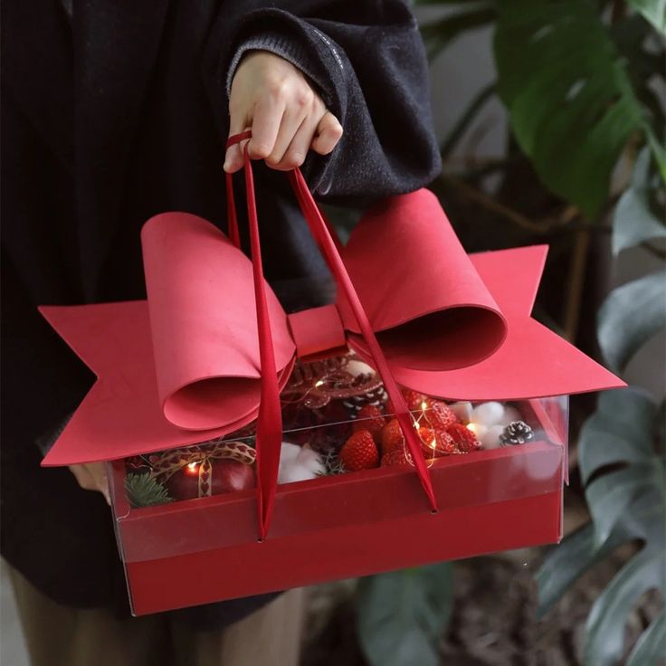 a person is holding a red box with two large paper bells in it and some candles inside