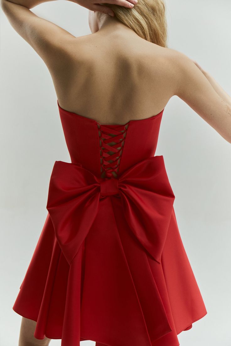 Introducing the Emily Dress with Bow: a stunning mini satin dress in a vibrant red color, designed to make a bold statement. This eye-catching dress features a dramatic maxi bow at the lower back, perfect for girls who love to stand out and make an impression. The Emily Dress is not only striking in design but also offers a perfect fit with adjustable lacing at the back. This ensures that you feel comfortable and confident throughout any special event. The vibrant red hue enhances its sophistica Formal A-line Dress With Satin Bow, Mini Dress With Bow For Gala, A-line Mini Dress With Bow For Prom, Evening Mini Dress With Detachable Bow, Sleeveless, Formal A-line Mini Dress With Bow Tie Back, Gala Mini Dress With Bow, A-line Evening Dress With Bow For Party, Sleeveless Evening Dress With Bow, Elegant A-line Mini Dress With Satin Bow