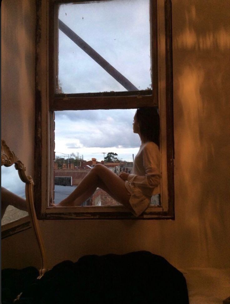 a woman sitting on the window sill looking out