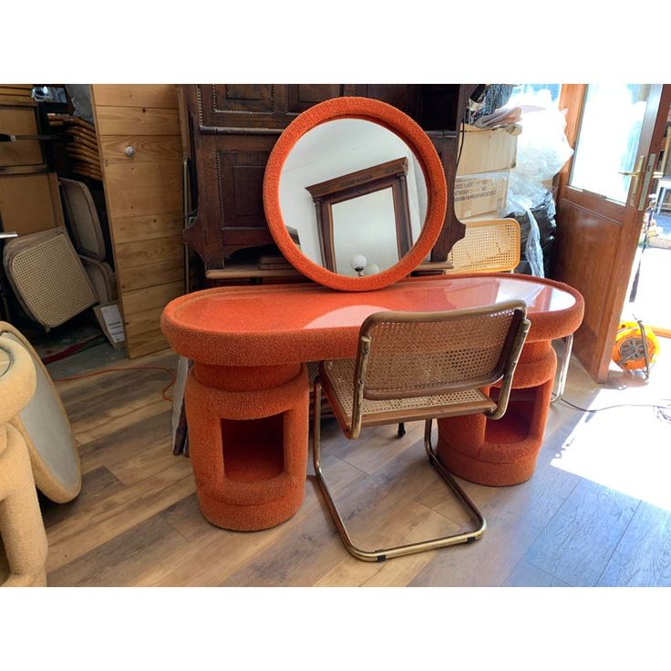 an orange table with two chairs and a round mirror